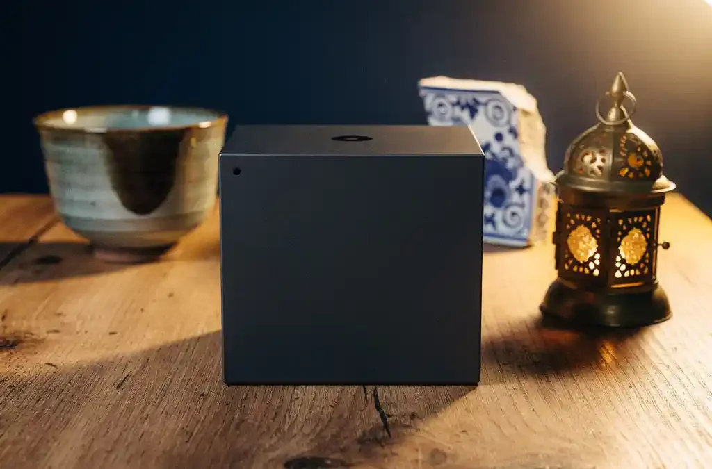 Consumer electronics box on wooden table surrounded by Japanese tea cup, Delft pottery shard, and brass Middle Eastern lantern in warm amber light.