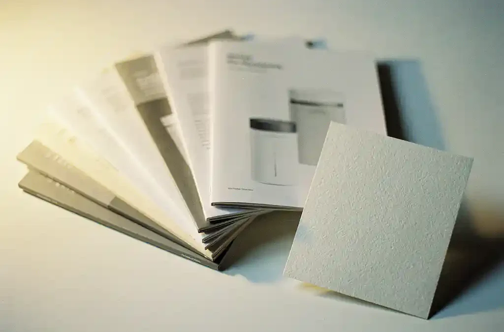 Opengeslagen producthandleiding op wit bureau met gestapelde manualen en mat textielpapier in warm studiolicht.